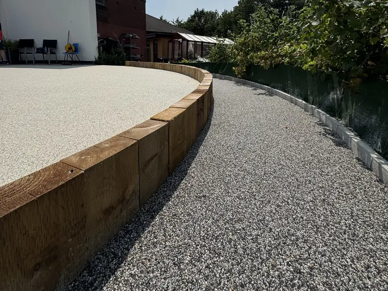Grey resin bound path curving beside a raised cream resin area edged with timber sleepers