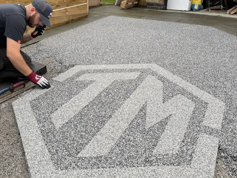 T&A Resin installer finishing a two tone hexagon logo inlay in a grey resin driveway